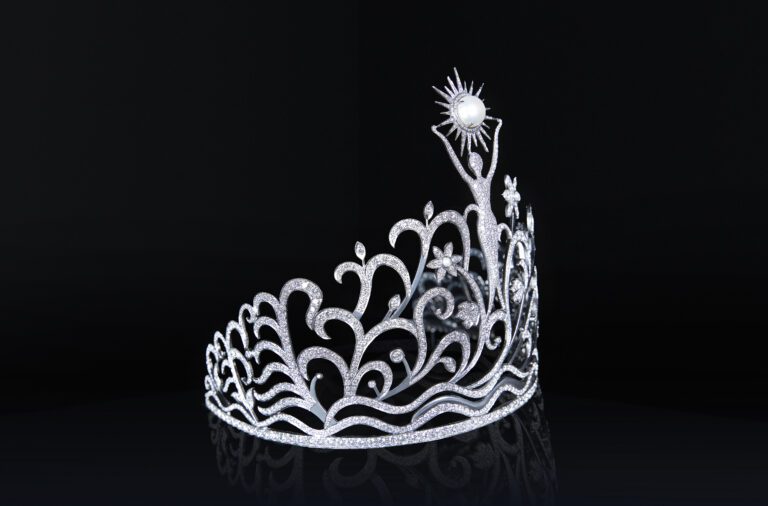 En el centro se encuentra la figura de la mujer — símbolo de la mujer puertorriqueña como esencia de la corona. En esta nueva versión, sus brazos ya no están hacia abajo; están abiertos y extendidos, dando la bienvenida al mundo.  Ese gesto transforma la corona en un símbolo de invitación, orgullo y conexión.